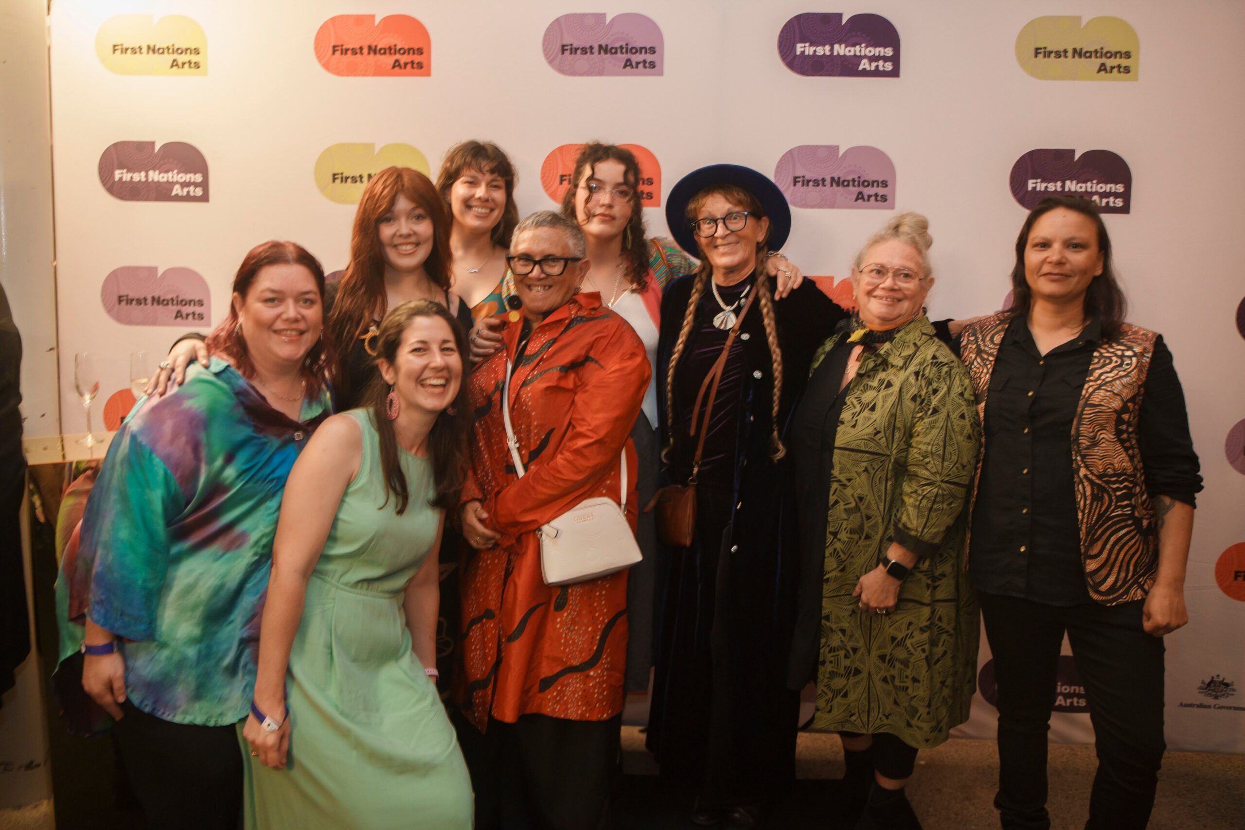 Group of people posing together in front of a First Nations Arts backdrop at an event.